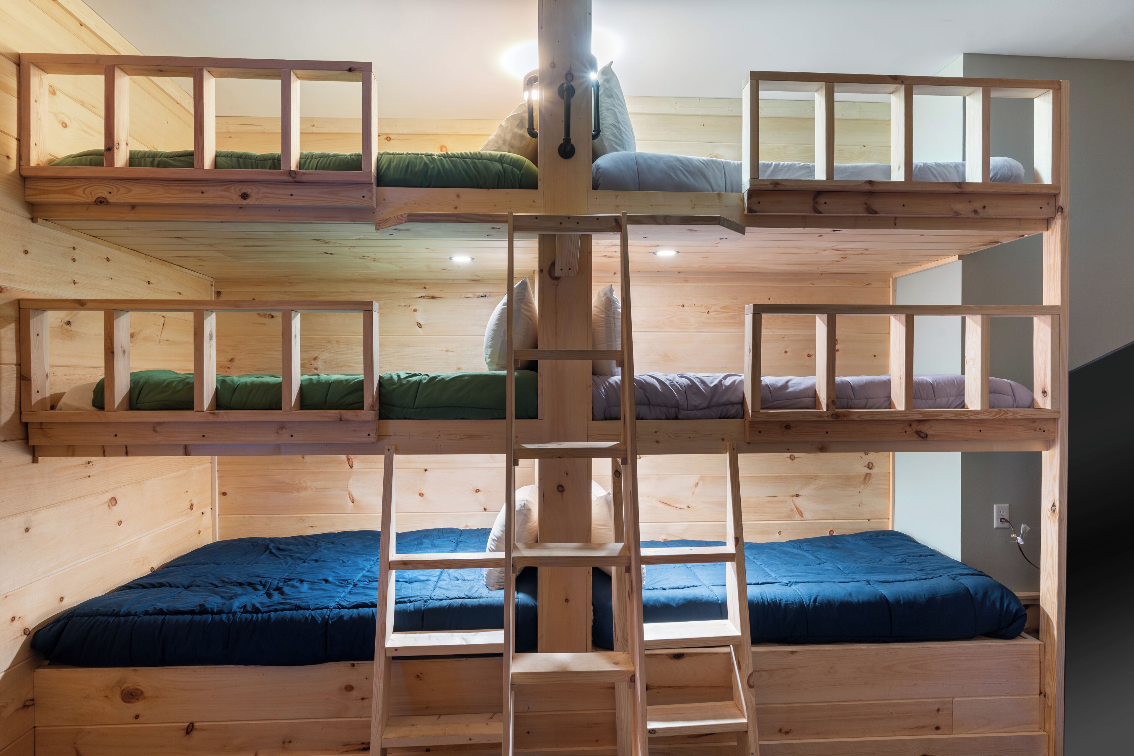 A multi-level bunk bed room with a central ladder, wooden walls, and a window.