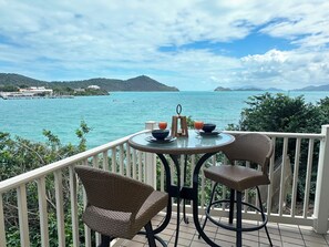 Un balcon avec des fauteuils en osier, une table ronde et une vue sur la mer et les îles lointaines.