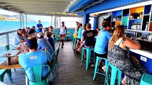 Un grupo de personas sentadas en mesas en la cubierta de un barco, con vista al mar.