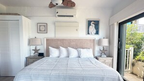 Un dormitorio con una cama grande, dos mesitas de noche, decoración con motivos de estrellas de mar, un ventilador de techo y vistas al exterior con vegetación.