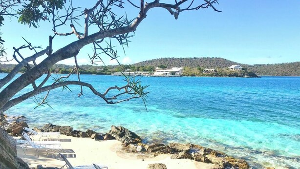 Una playa con agua azul cristalina, costa rocosa y sillas de descanso.