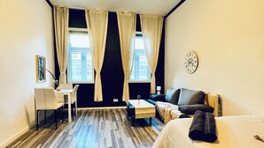 Une chambre d’hôtel avec un lit, un bureau, une chaise, un canapé et une horloge au mur.