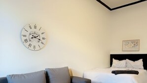Une chambre d’hôtel moderne avec un canapé, un lit, une table de chevet ornée d’un cactus et une horloge murale.