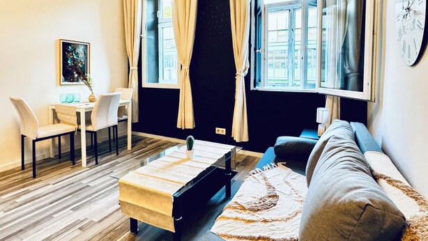 Un salon moderne comprenant un canapé, une table basse, une table à manger avec des chaises et une grande fenêtre avec des rideaux.