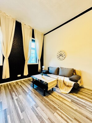 Une pièce avec un plancher en bois, un canapé, une table avec une plante et une horloge murale.