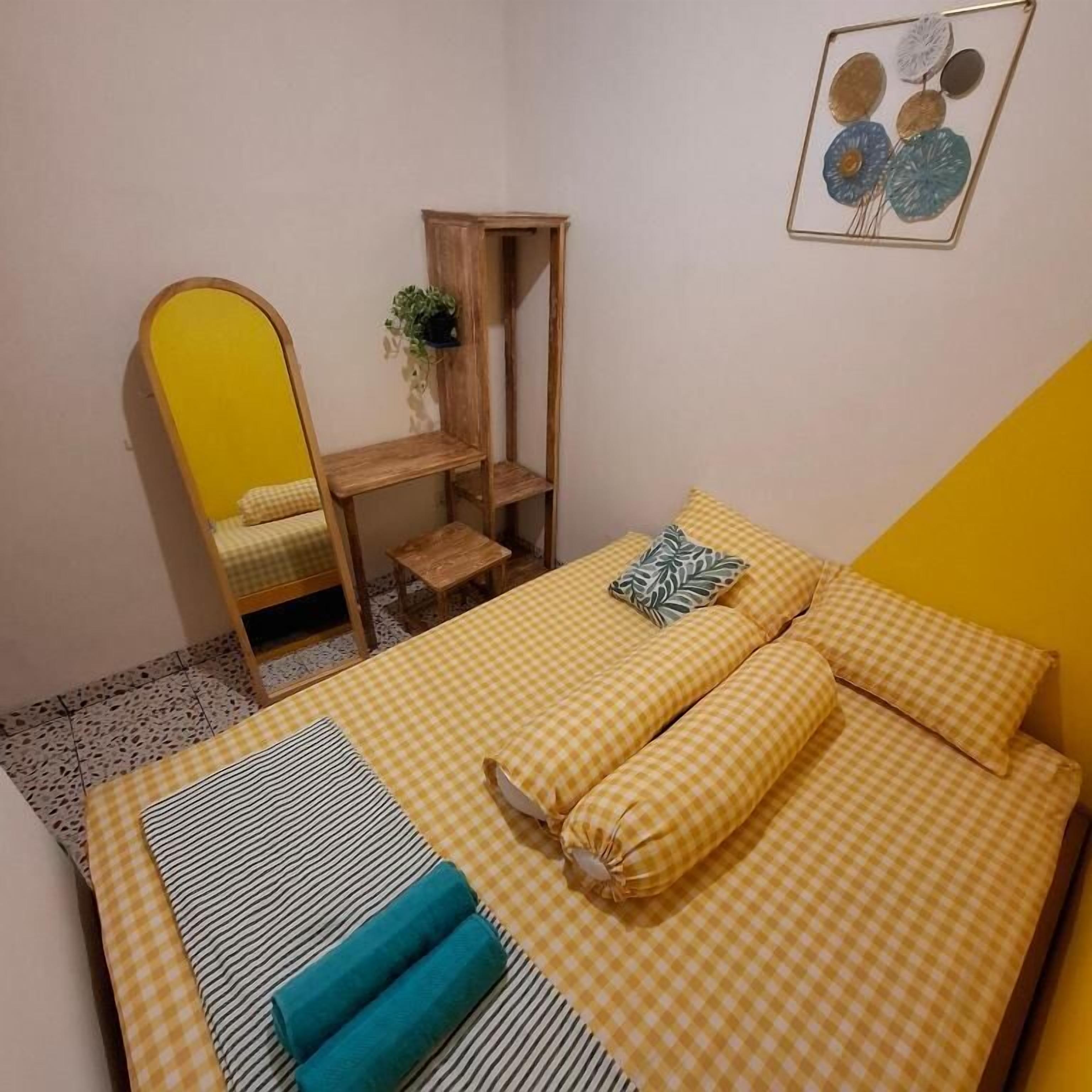 Un dormitorio con cama, un espejo, un estante de madera pequeño y un adorno en la pared.