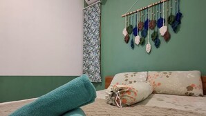 Ein Zimmer mit einem Bett, einem aufgerollten türkisfarbenen Handtuch und zwei Frangipani-Blumen auf einem strukturierten Teppich.