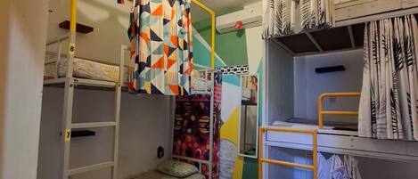 A dormitory room with bunk beds, a patterned curtain, and a small shelf.