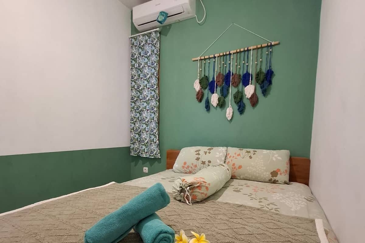 A neatly made bed with floral bedding, a teal towel, and a tropical flower on the bed.