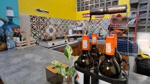 Eine Küche mit gelber Wand, einer gefliesten Spritzschutzleiste und einer Kaffeemaschine. Auf der Arbeitsplatte stehen Flaschen und in einem Glasgefäß steht eine Pflanze.