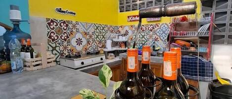 A kitchen with a yellow wall, a tiled backsplash, and a coffee machine. There are bottles on the counter and a plant in a glass container.