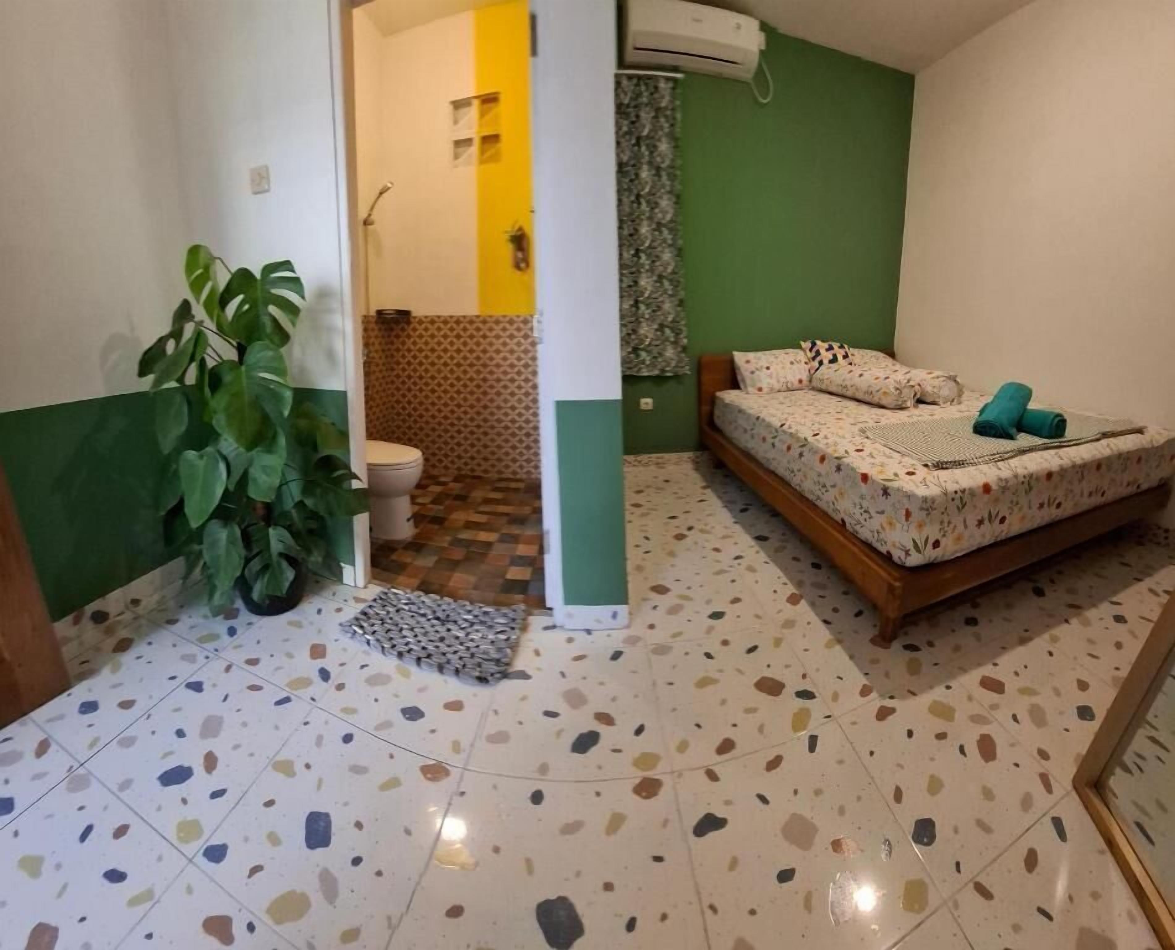 A small room with a bed, a potted plant, and a bathroom with a toilet and shower.