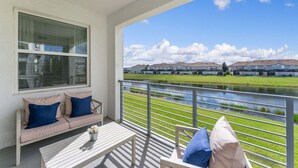 Ein Balkon mit einer weißen Bank und Kissen mit Blick auf eine Rasenfläche und eine Häuserreihe.