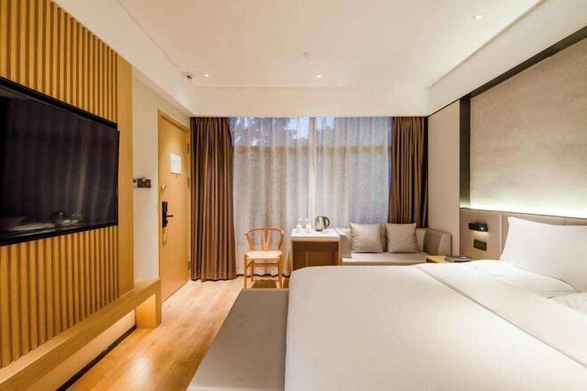 Ein modernes Hotelzimmer mit einem großen Bett, einem Fernseher, einem Schreibtisch mit Stuhl und einem Fenster mit Vorhängen.