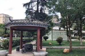 Un belvédère doté d’un toit à l’architecture traditionnelle, entouré d’un jardin aménagé avec des arbres et un chemin pavé.