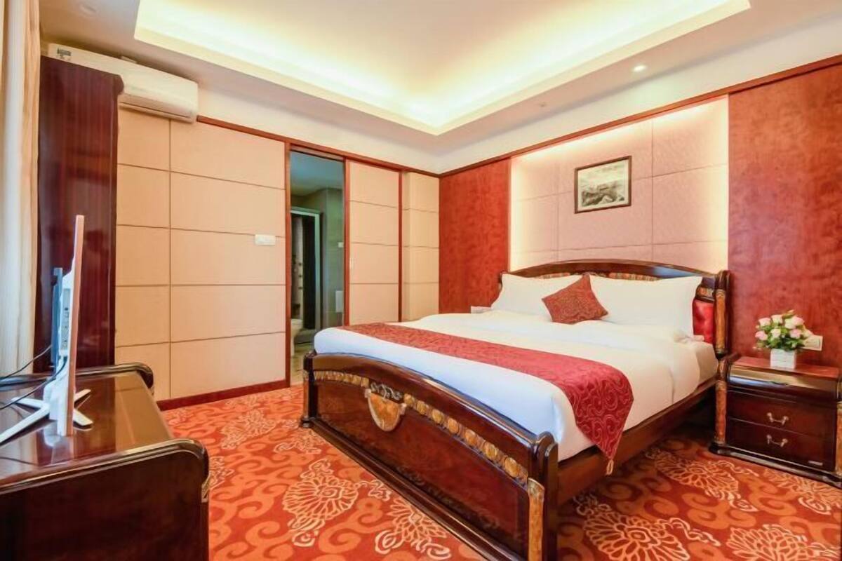 Ein Hotelzimmer mit einem großen Bett, einem Schreibtisch mit Stuhl, einem Fernseher und einem Kleiderschrank.