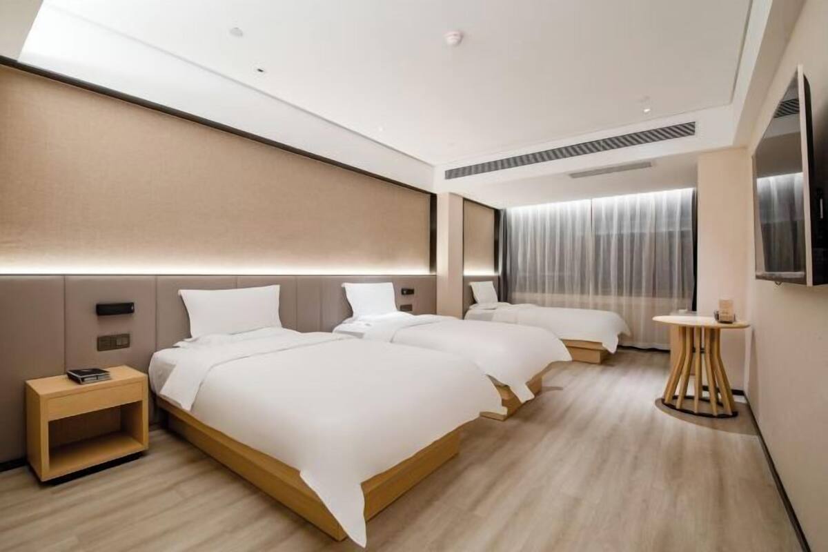 Ein modernes Hotelzimmer mit zwei Betten, einem kleinen Nachttisch, einem runden Tisch und einem großen Fenster mit Vorhängen.