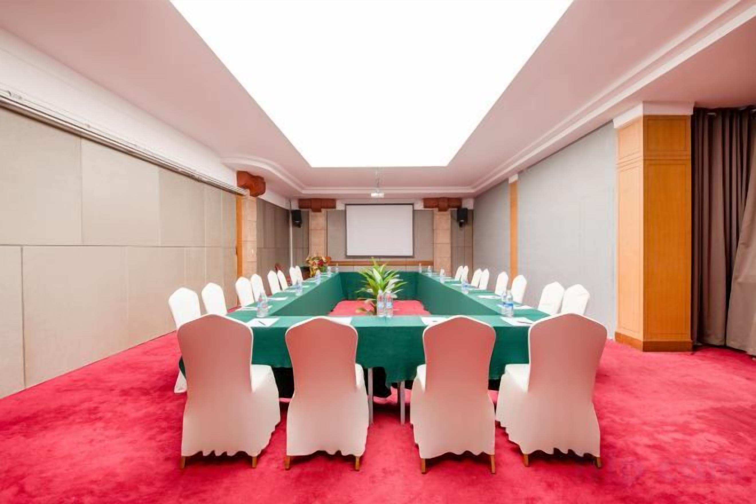 A conference room with a long table, white chairs, and a red carpet.