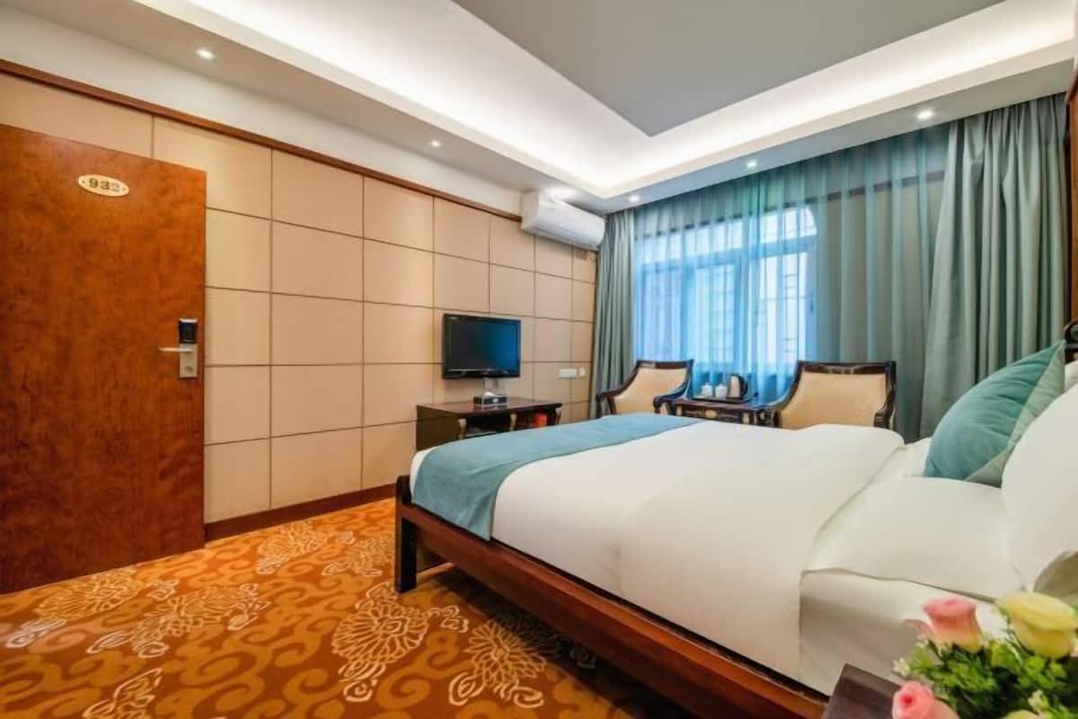 Ein Hotelzimmer mit einem Bett, einem Fernseher, einem Schreibtisch und einem Fenster mit Vorhängen.