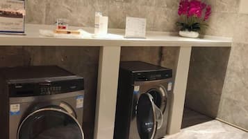 A laundry area with two front-loading washing machines under a white counter, a potted plant, and a small sign.