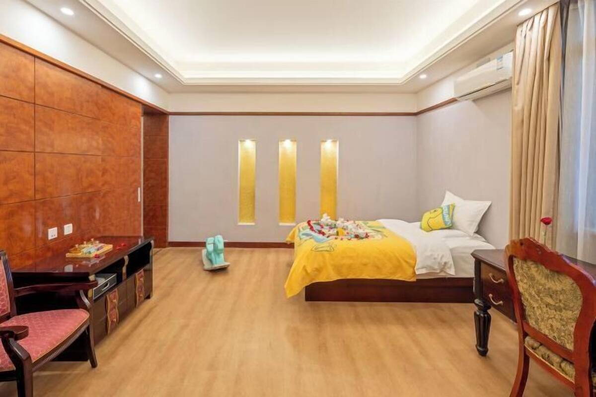 Ein Hotelzimmer mit Holzboden, einem Bett mit gelber Decke, einem Schreibtisch mit Stuhl und einer Wandverkleidung.