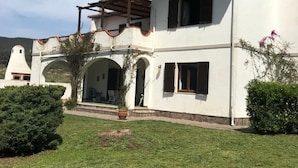 Une maison à deux étages dotée d’un patio couvert, d’un petit jardin et surplombant un paysage montagneux.
