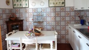 Un coin repas avec une table blanche, des chaises et un luminaire suspendu. Le mur est décoré d’illustrations botaniques encadrées, et un pare-feu en carreaux se trouve derrière la table.