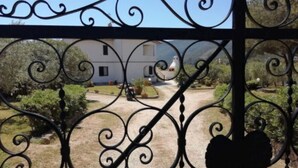 Une entrée fermée par un portail en fer forgé, qui mène à un bâtiment à la façade blanche et au toit rouge.
