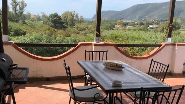 Une terrasse extérieure avec une table et des chaises, un barbecue et une vue panoramique sur les collines et les arbres.