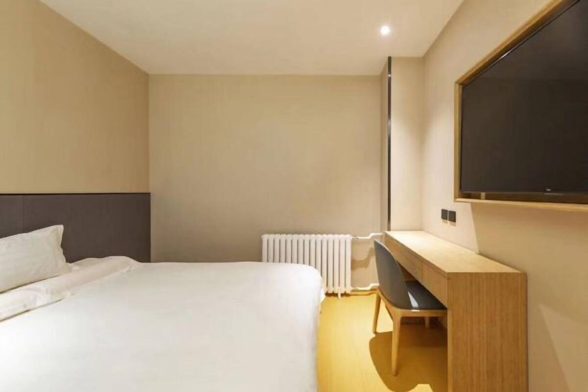 A modern hotel room with a bed, a desk, a chair, a television, and a radiator.
