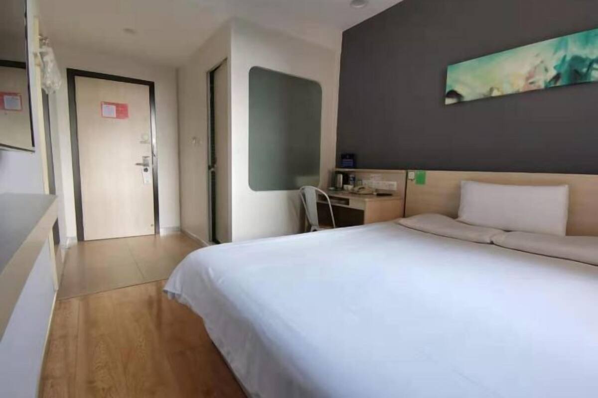 A hotel room with a bed, a desk, a chair, a painting on the wall, and a door.