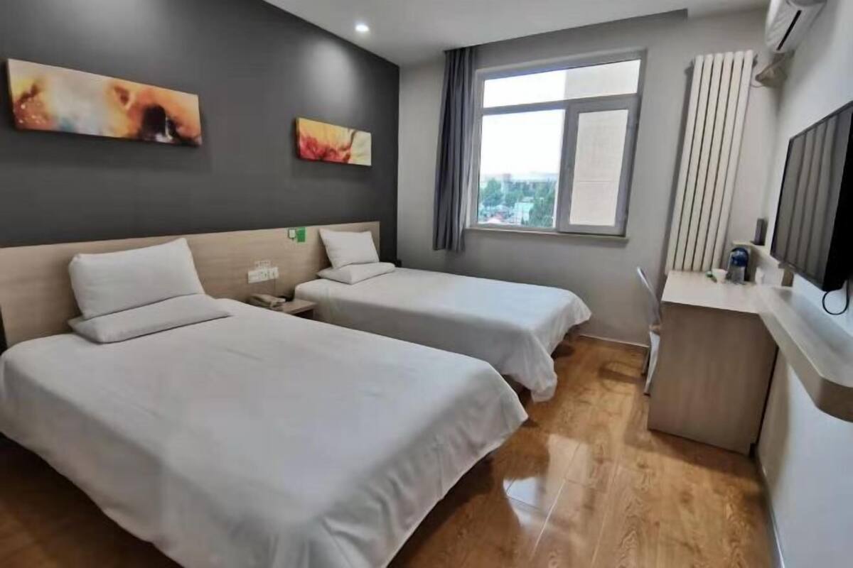 A hotel room with two beds, a window, a desk, and artwork on the wall.