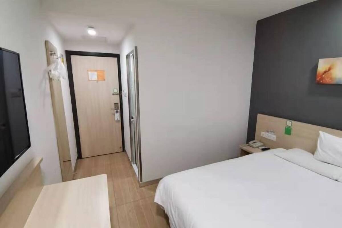 A hotel room with a bed, a bedside table, a nightstand, a TV, and a door leading to another room.