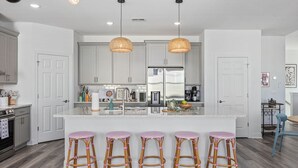 Een moderne keuken met witte kasten, een centraal eiland met barstoelen en hanglampen.