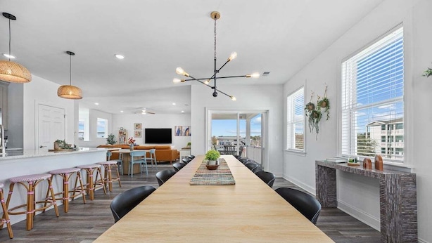 Een ruime keuken met een lange houten tafel, zwarte stoelen en een centraal eiland met barstoelen.