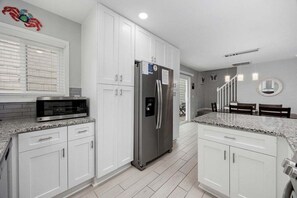 A kitchen with white cabinets, a stainless steel refrigerator, a microwave, and granite countertops. - Blue Pearl | Affordable 3BR Home | Walk to Beach (North Myrtle Beach)
