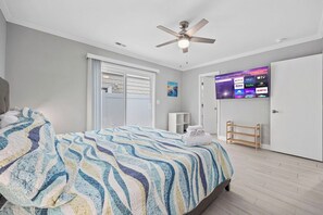 Une chambre à coucher comprenant un lit, un ventilateur de plafond, un téléviseur permettant d’accéder à des services de diffusion en continu, une porte et une fenêtre.