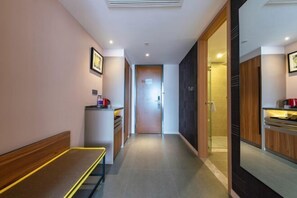 A hotel corridor with a bench, a refrigerator, a door leading to a bathroom, and a mirror reflecting the room. - Homeinn Plus Hotel (Qingdao Licun Subway Station Pedestrian Street) (Qingdao)