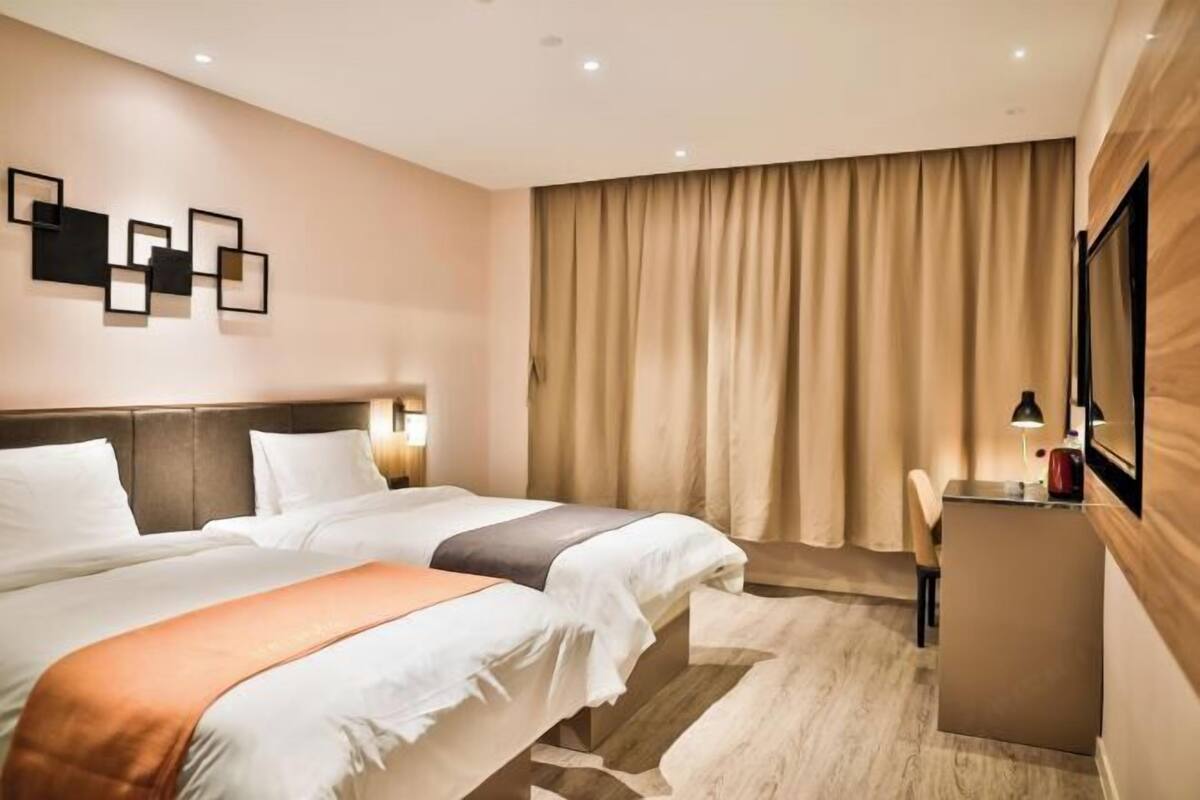 A hotel room with two beds, a desk, a chair, a TV, and a wall-mounted artwork.
