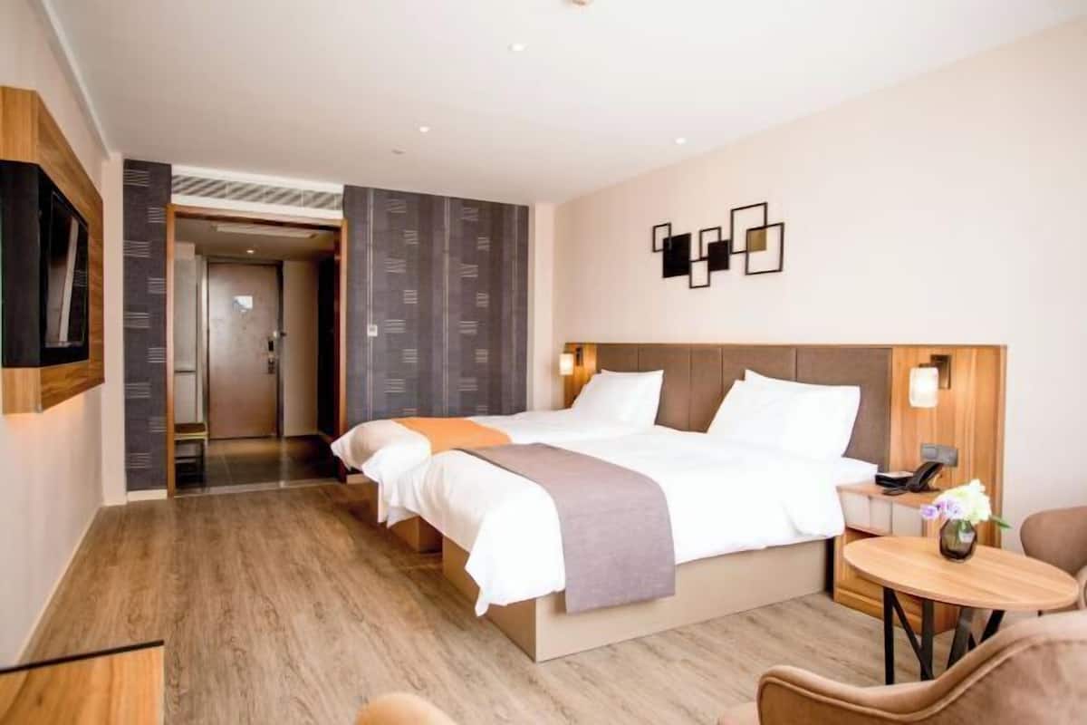 A hotel room with a large bed, a bedside table, a chair, and a small table with a vase.