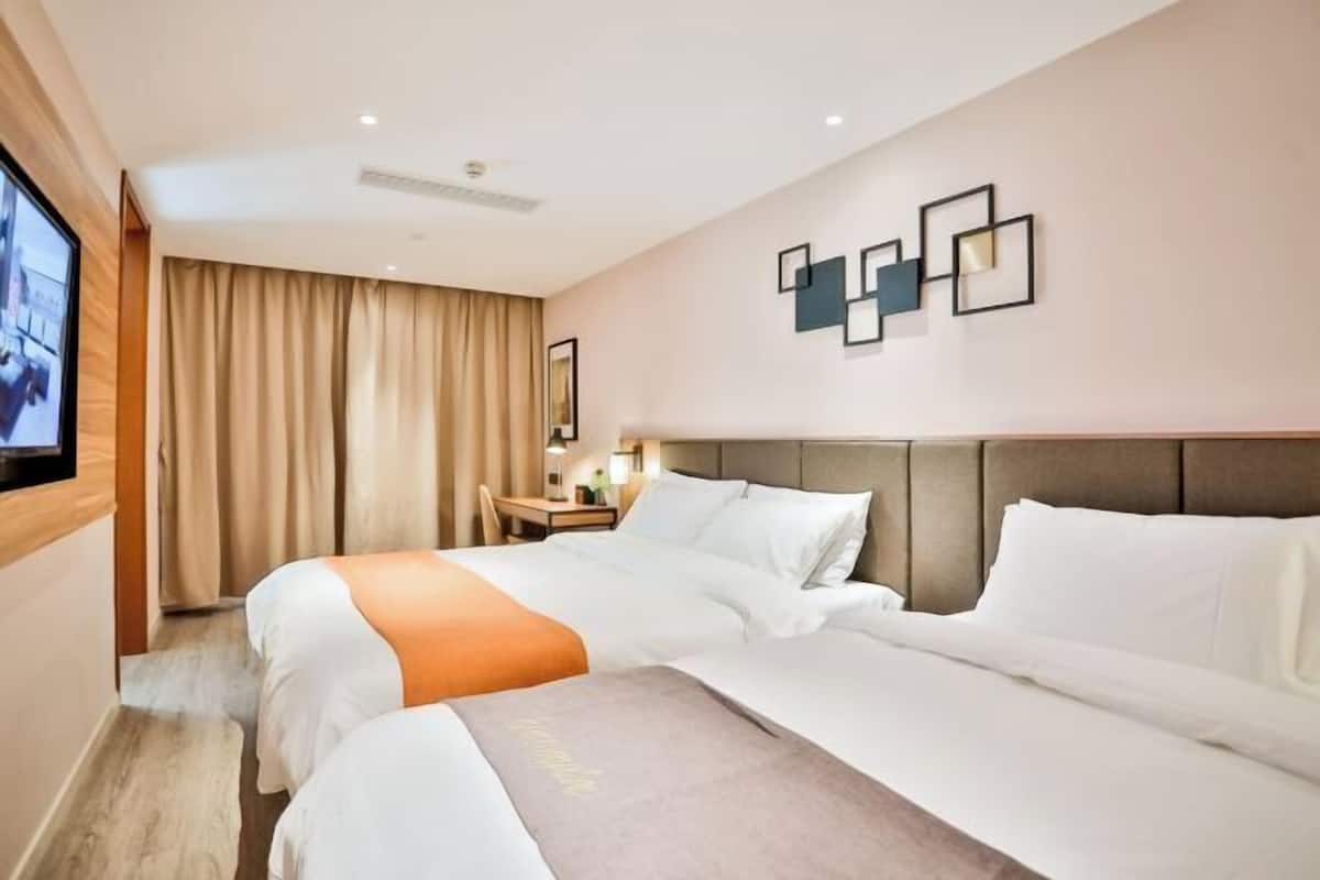 A hotel room with two beds, a TV, a desk with a lamp, and a wall with framed pictures.