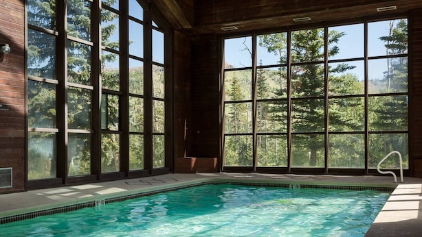 Une piscine à l’eau claire, entourée de grandes fenêtres qui offrent une vue sur les arbres.