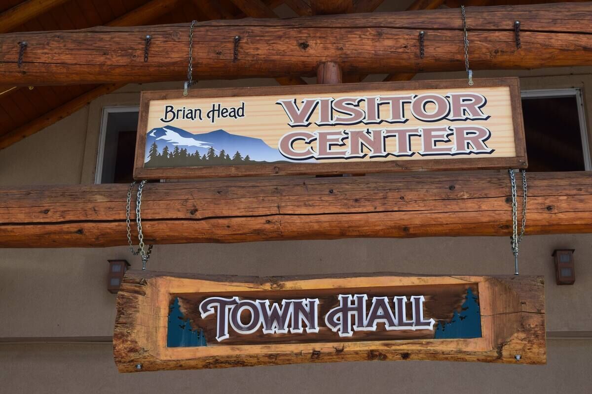 A wooden sign for the Brian Head Visitor Center and Town Hall, featuring a mountain and forest illustration.