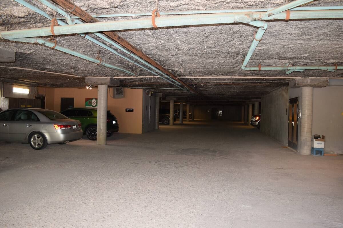 Un parking souterrain faiblement éclairé, avec des piliers en béton et des tuyaux métalliques.