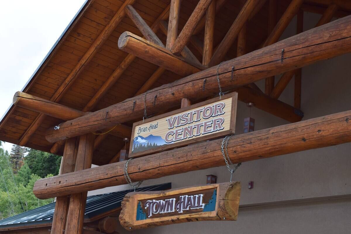 A wooden sign with "Visitor Center" and "Brian Head" written on it, hanging from a wooden beam.