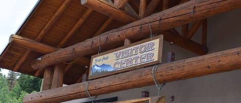 A wooden sign with "Visitor Center" and "Brian Head" written on it, hanging from a wooden beam.