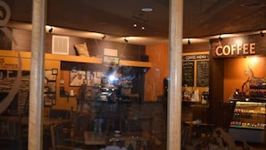L’intérieur d’un café accueillant, avec un tableau des prix bien visible, un espace salon et un présentoir à café.