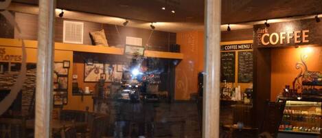 L’intérieur d’un café accueillant, avec un tableau des prix bien visible, un espace salon et un présentoir à café.