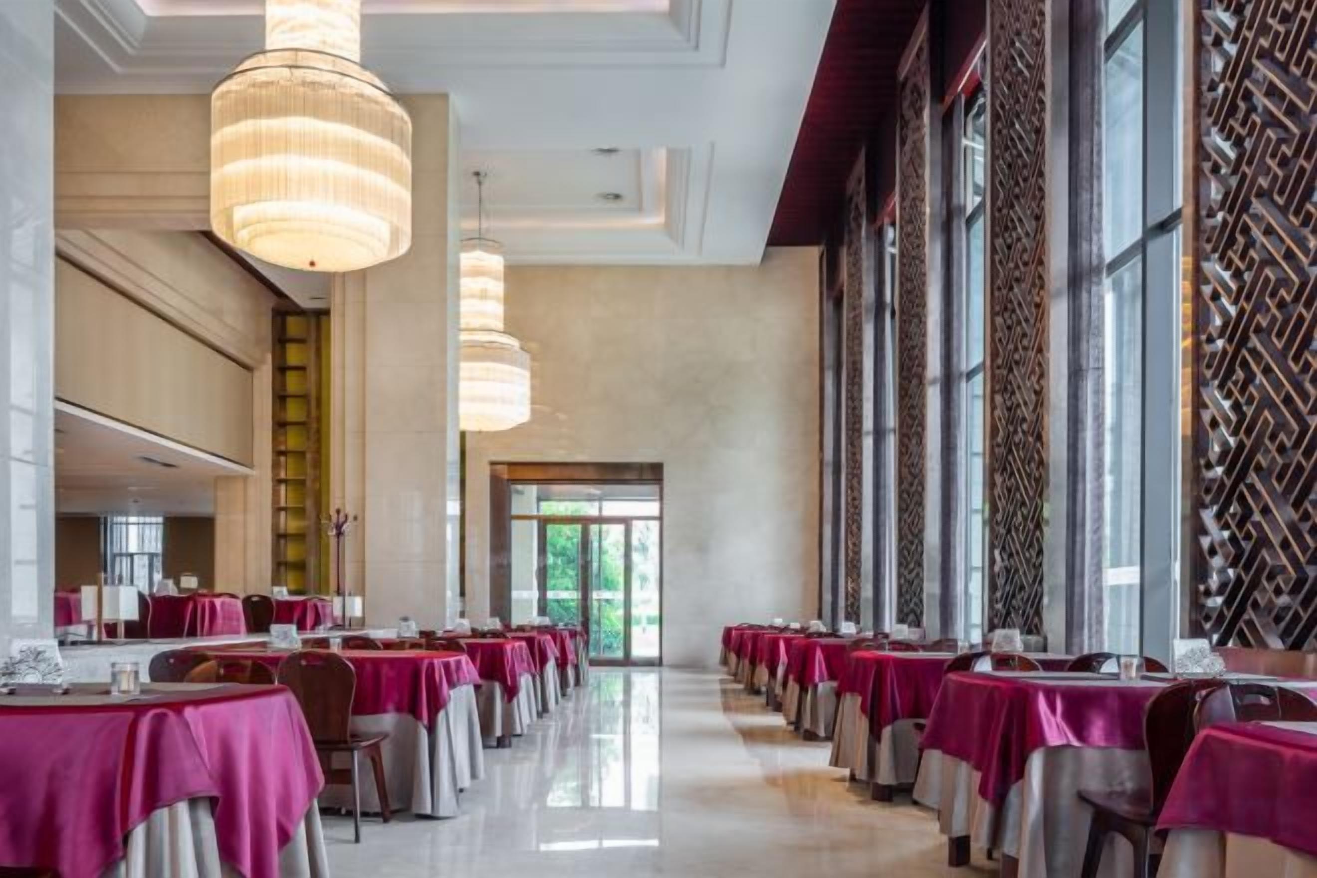 A long dining hall with tables covered in tablecloths, large windows, and hanging light fixtures.