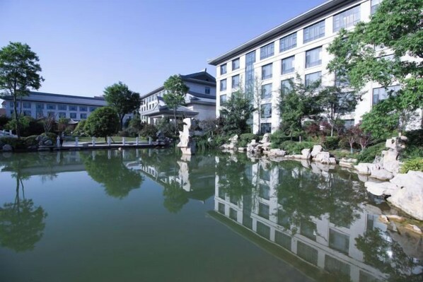 A hotel with a large reflective pond, surrounded by trees and a white building with multiple windows.